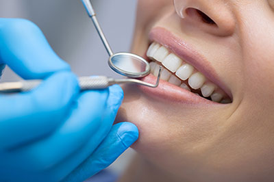 A dental professional performing a teeth cleaning procedure on a patient s mouth using specialized equipment, with the patient wearing protective gloves and a blue surgical gown