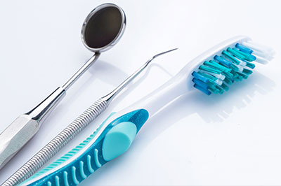 Dental instruments including a pair of tweezers, a toothbrush with blue bristles, and other dental tools on a light background