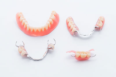Three pairs of dentures with pink gums, displayed on a white background