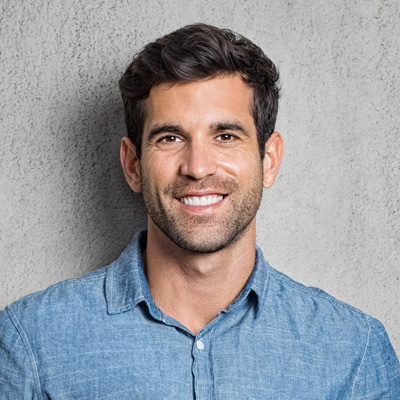 A man in a blue denim shirt smiling at the camera against a plain grey background