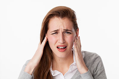 A woman with her hand on her head, appearing to be experiencing discomfort or pain, possibly related to an ear issue