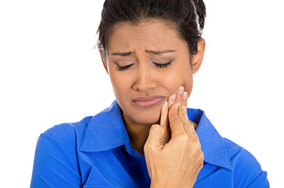 A woman with a concerned expression, holding her face with one hand while looking at something with the other, possibly related to dental care or health concerns